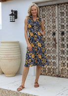Woman wearing midi length, sleeveless  cotton dress with collar and pockets in black based retro floral print.