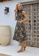 Woman standing with hand in pocket wearing a collared, sleeveless 100% cotton dress with button-up front in retro floral print