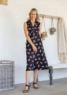Woman wearing midi length, sleeveless  cotton dress with collar and pockets in black based floral print.