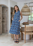 Woman wearing midi length, sleeveless  cotton dress with collar and pockets in navy based floral print.