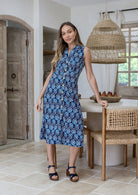 Woman wearing a sleeveless floral cotton dress with button through front, pockets and a-line skirt.