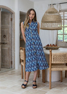 Woman wearing midi length, sleeveless  cotton dress with collar and pockets in navy based floral print.