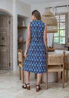 Woman standing backwards wearing a midi length floral print dress with button through front, pockets and a collar.