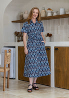 Woman wearing 100 percent cotton button through shirt dress with collar and short sleeves, in a navy based floral print. 