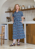 Model standing with both hand in pockets wearing a floral printed shirt dress with detachable fabric belt and short sleeves 