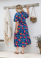 Model standing backwards wearing a floral printed shirt dress with detachable fabric belt and short sleeves 