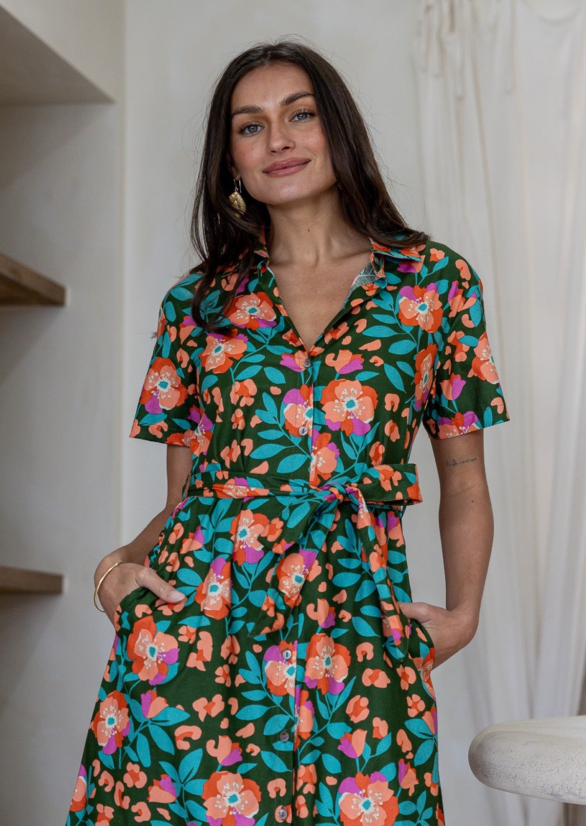 Model stands wearing a shirt style button through cotton dress with collar and a removable waist tie.
