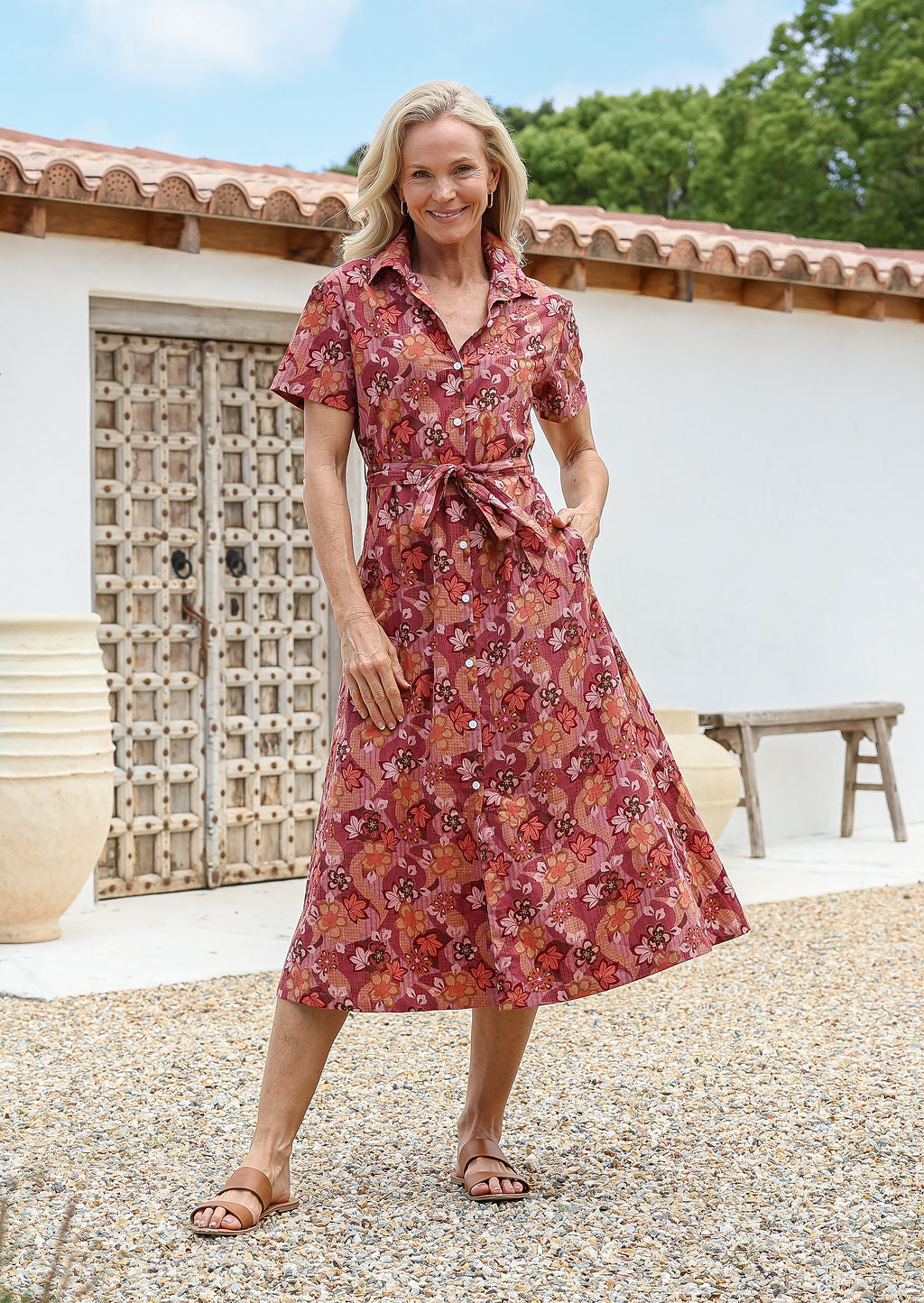 Woman wears 100% cotton warm toned button through shirt style dress with pockets, collar, short sleeves and a fabric waist tie.