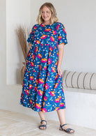 Woman posing in three tiered cotton midi length dress with short sleeves, in blue based graphic floral print