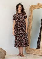 Woman wearing a 100% cotton, midlength black dress featuring three tiered design, short sleeves, high round neckline and pockets