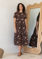 Woman wearing a black based floral cotton midi length dress with tiered skirt and short sleeves