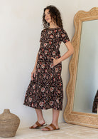 Woman wearing a relaxed fit printed black cotton dress with tiered design, standing next to a large mirror