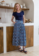 Woman wearing a navy basic top and floral button through shin length cotton skirt with box pleats, belt loops and pockets.