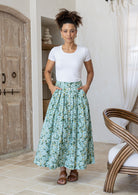 Woman wearing a white basic top and floral button through shin length cotton skirt with box pleats, belt loops and pockets.