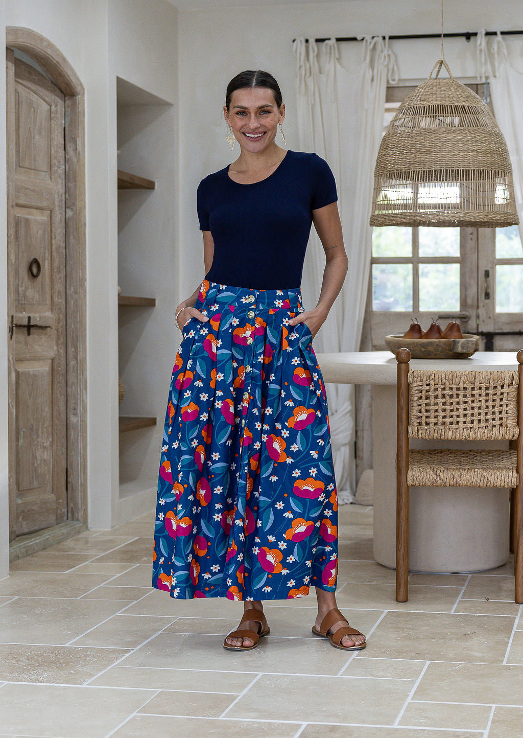 Woman standing with both hand in pockets wears 100% cotton button through skirt in royal blue based floral print. 