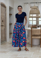 Woman standing with both hand in pockets wears 100% cotton button through skirt in royal blue based floral print. 
