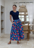 Woman wearing a basic top and floral button through shin length cotton skirt with box pleats, belt loops and pockets.