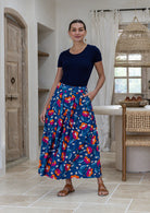 Woman stands wearing a floral print, shin length cotton skirt with button through front and box pleats.