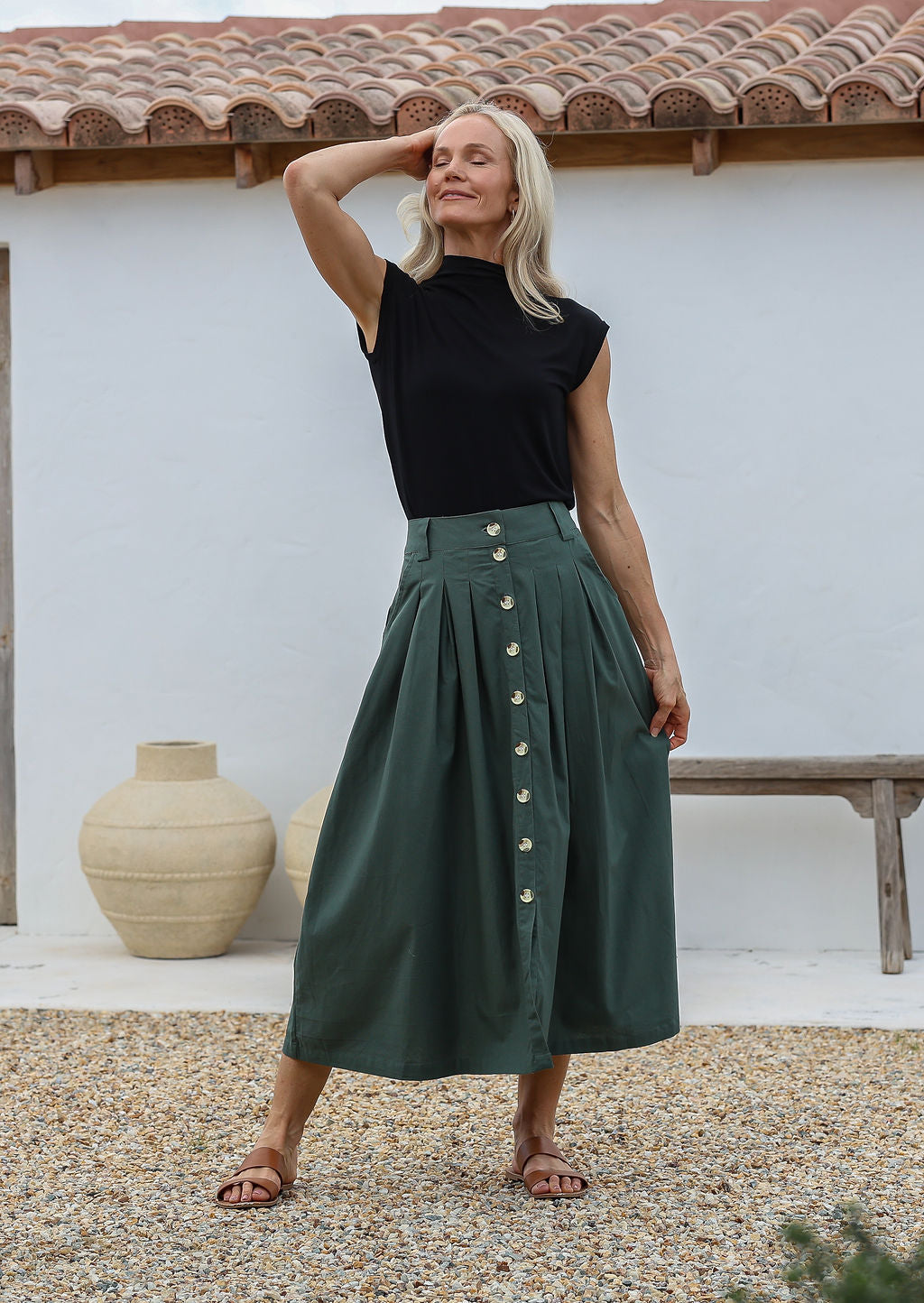 Woman posing in a tailored long cotton skirt with button through front, box pleats and belt loops.