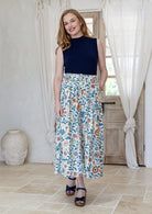 Woman wearing a navy basic top and floral button through shin length cotton skirt with box pleats, belt loops and pockets.