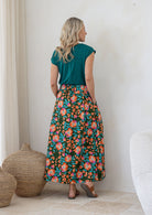 Woman stands backwards wearing a basic top and floral print, shin length cotton skirt with button through front and box pleats.