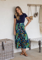 Woman wearing a navy basic top and floral peacock button through shin length cotton skirt with box pleats, belt loops and pockets.