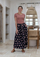 Woman stands wearing a basic top and floral print, shin length cotton skirt with button through front and box pleats.