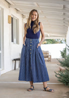Woman standing with both hand in pockets wears 100% cotton button through skirt in navy based white striped print. 