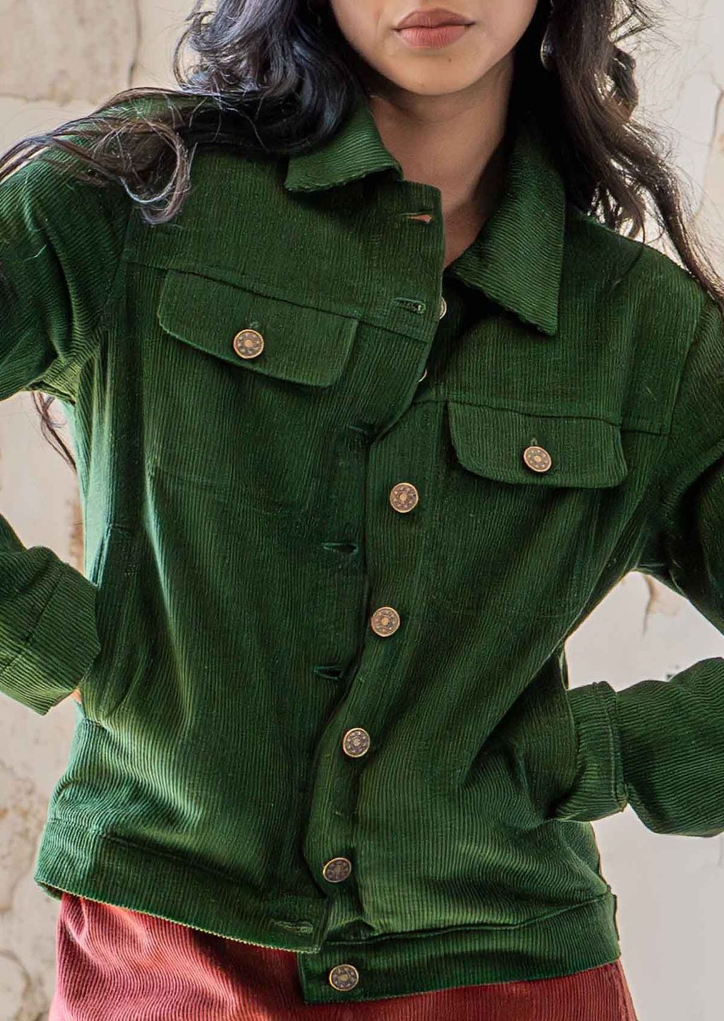 Close up of woman wearing green brass button down corduroy jacket with hands in pockets 