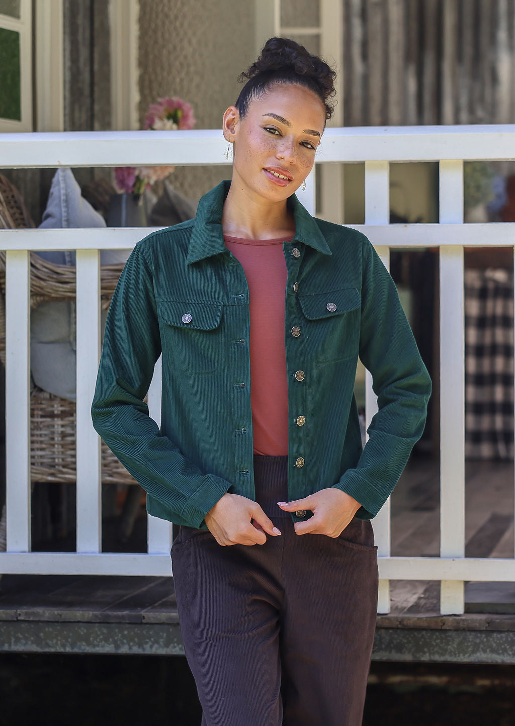 Woman wearing a jacket in deep, luxurious, deep blue green standing against a white railing