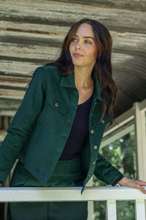 Woman in a corduroy jacket standing on a porch with a rustic background
