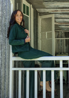 Woman in a green outfit sitting on a white railing inside a building.