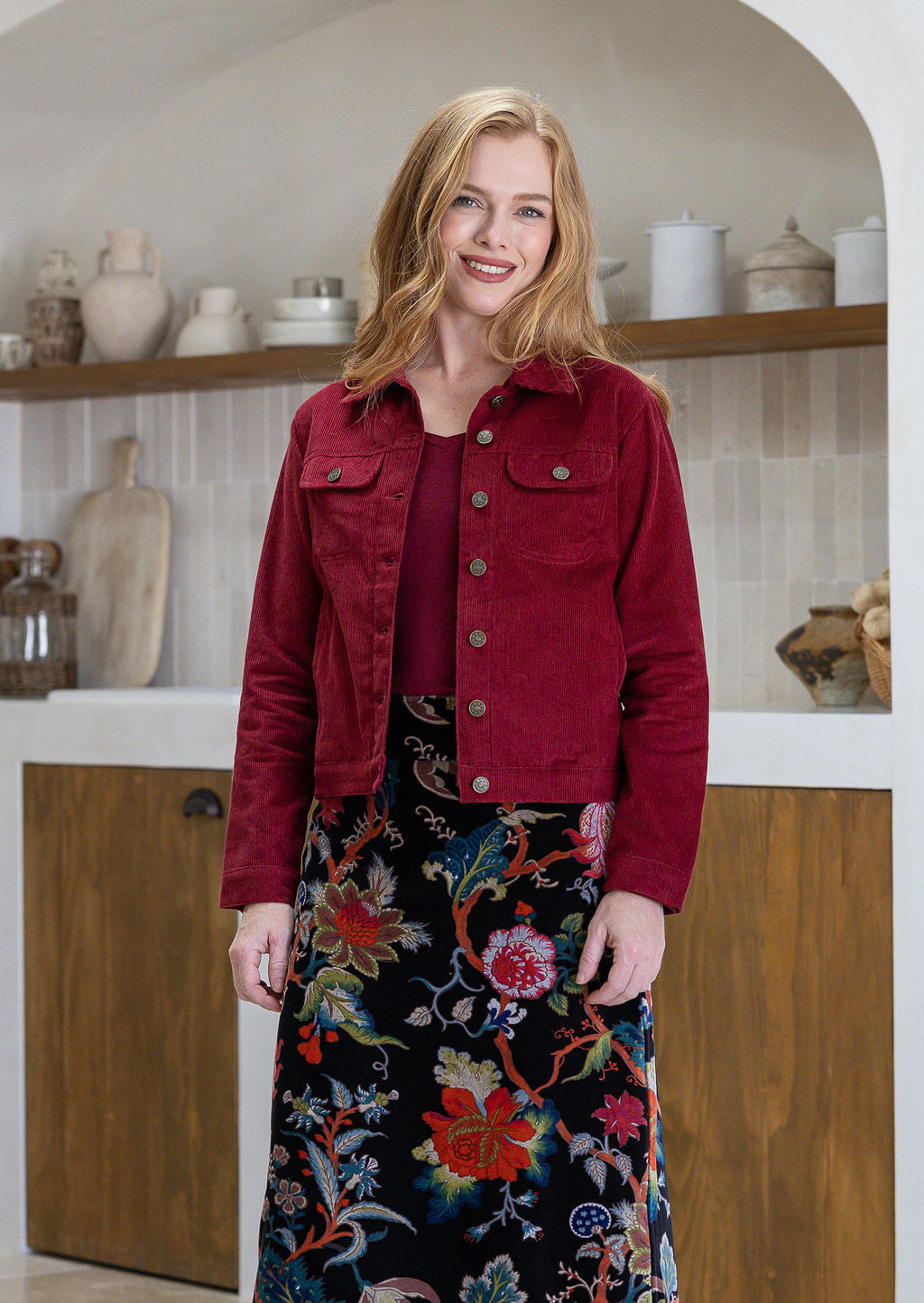 Woman wearing a red cotton corduroy jacket and floral velvet skirt in a kitchen setting