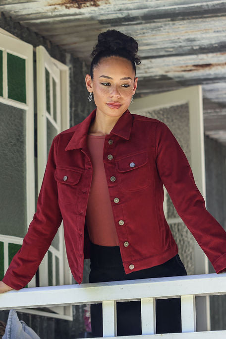Woman wearing a corduroy jacket standing on a porch with a rustic building in the background