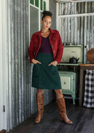Woman in a cotton corduroy jacket and green skirt standing in a rustic kitchen.