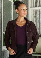 Woman wearing a dark brown cotton corduroy jacket with brass buttons over a purple top