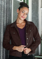 Woman wearing a brown cotton corduroy jacket with brass buttons and breast pockets over a purple top