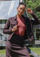 Woman wearing a brown cotton corduroy jacket and skirt, paired with a pink top, in front of a wooden fence