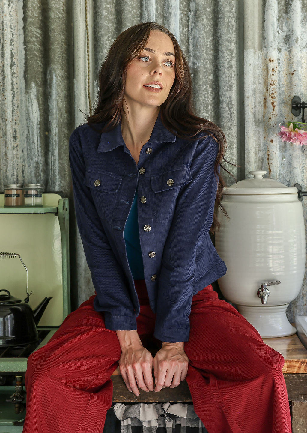 Woman in a navy blue jacket and pants sitting on a wooden stool in a rustic kitchen.
