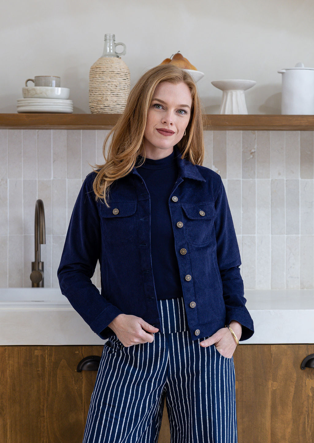 Woman wearing a deep, rich, and slightly muted navy blue jacket with brass buttons and front pockets