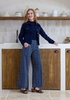 Woman in a kitchen wearing a navy jacket and striped pants.