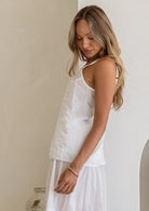 Side view of model wearing white lightweight cotton cami with V-neckline, adjustable spaghetti straps and  picot trim