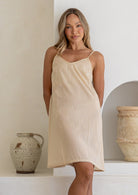 Beige cotton slip for undergarment with thin straps and lace hem, on a model standing against a wall.
