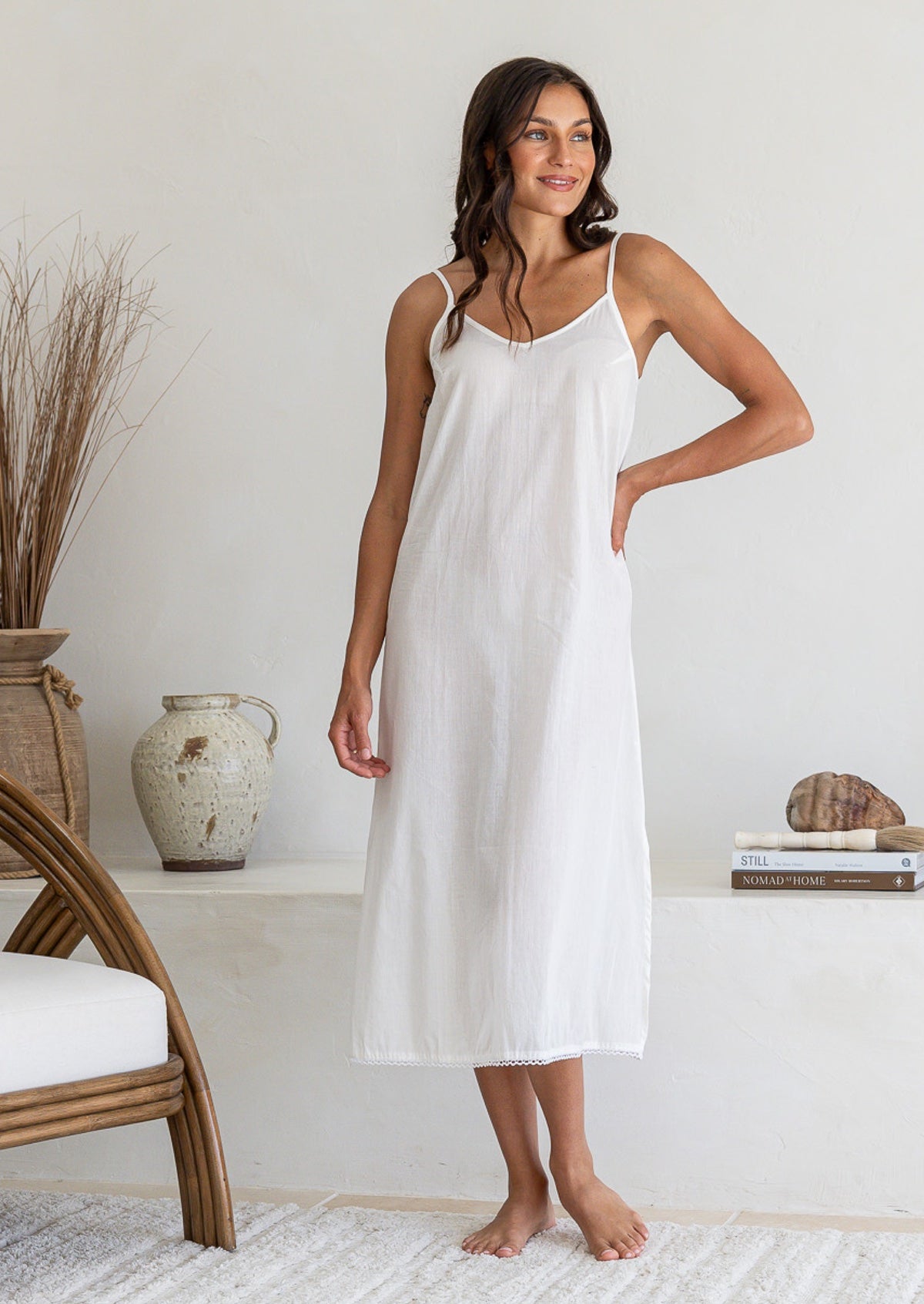 Woman poses in white lightweight cotton maxi slip with V-neckline, bust darts, side splits and picot trim hem