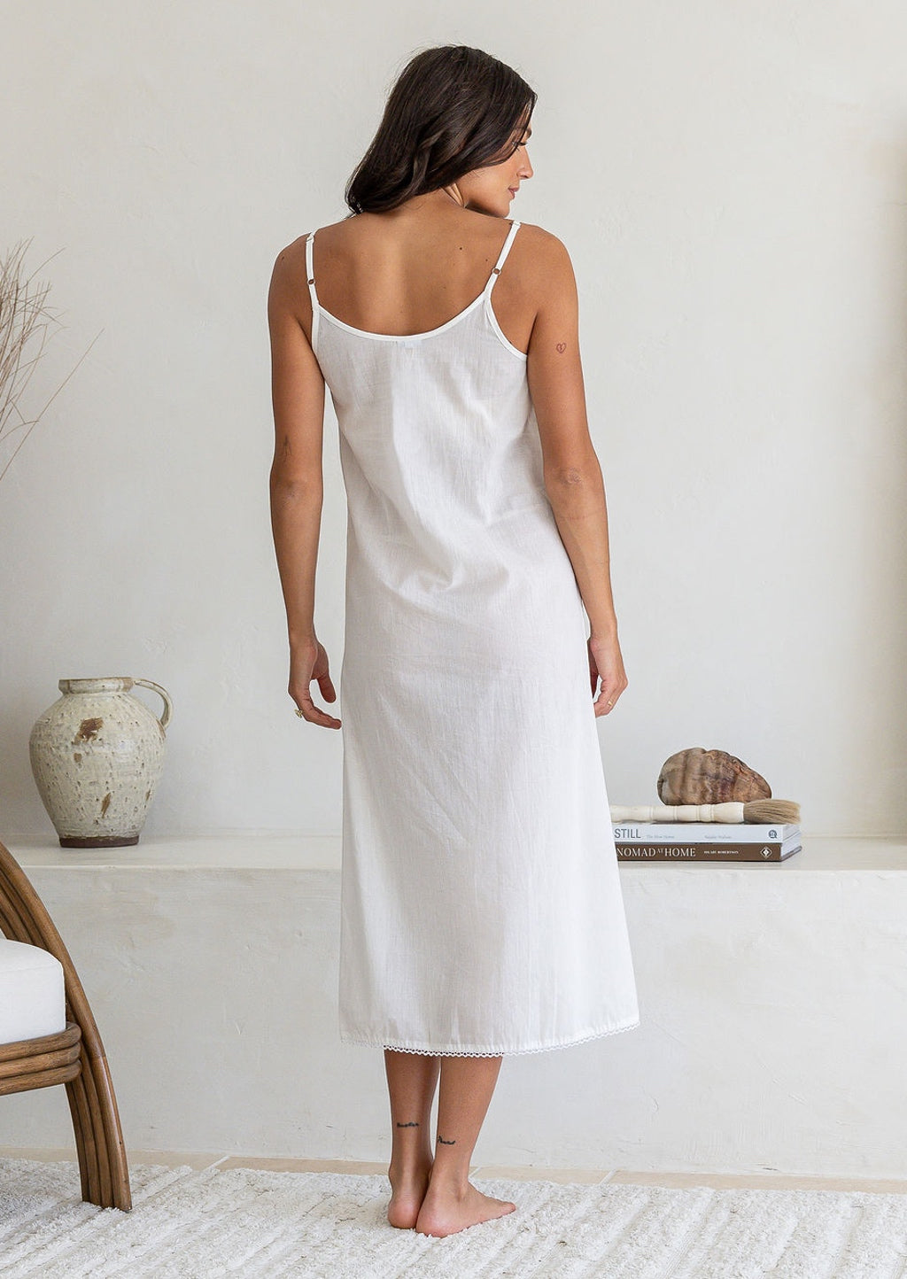 Back view of woman wearing white lightweight cotton maxi slip with adjustable spaghetti straps, side splits and picot trim hem