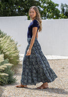Model standing sideways wearing a three tiered, cotton maxi skirt with plain basic top