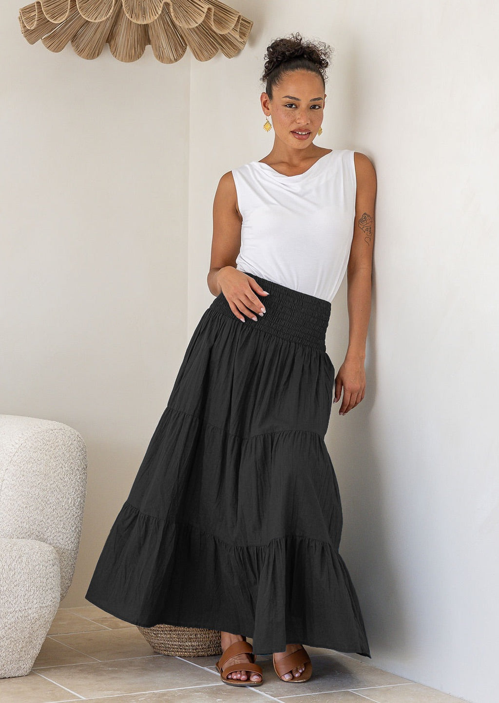 Woman wearing a white singlet top and black cotton tiered maxi skirt with wide ruched waistband