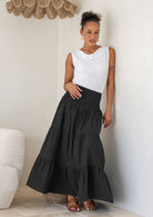 Woman wearing a white singlet top and black cotton tiered maxi skirt with wide ruched waistband