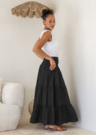 Woman standing side on wearing a white singlet top and black cotton tiered maxi skirt with wide ruched waistband