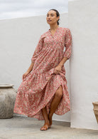 Woman wearing a 100% cotton rose pink  based floral dress standing against a white wall.